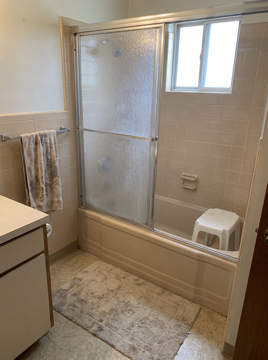 The old bathroom: a tub with sliding glass doors, and the plastic stool the homeowner had started using to shower.